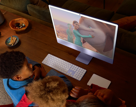 Devant une table, trois jeunes regardent un film sur un iMac avec Magic Keyboard et Magic Trackpad assortis