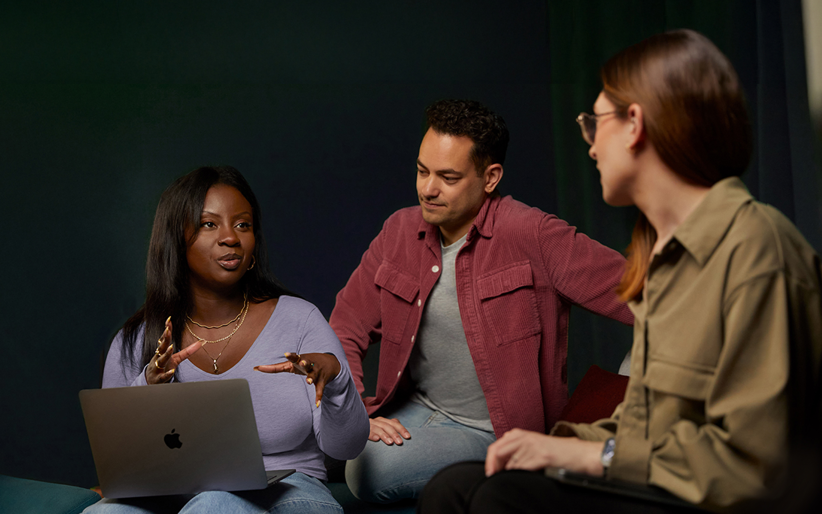 Três funcionários de uma equipe de software e serviços conversando em um sofá, e uma está com um MacBook