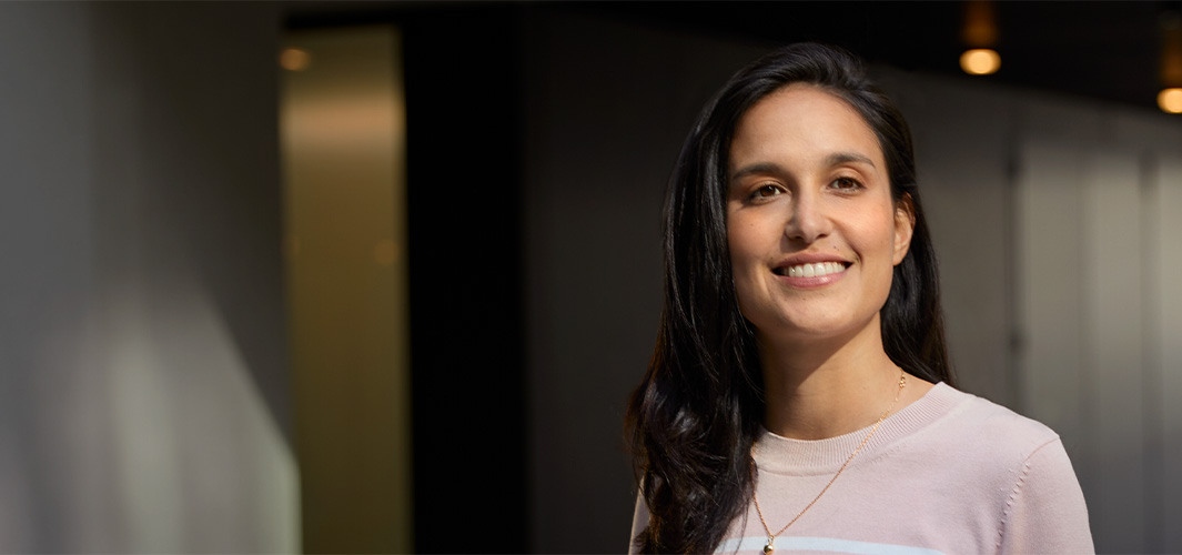 Camila sorri de pé em um escritório.
