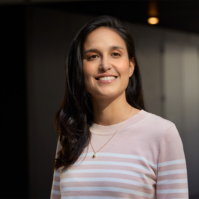 Camila sorri de pé em um escritório.