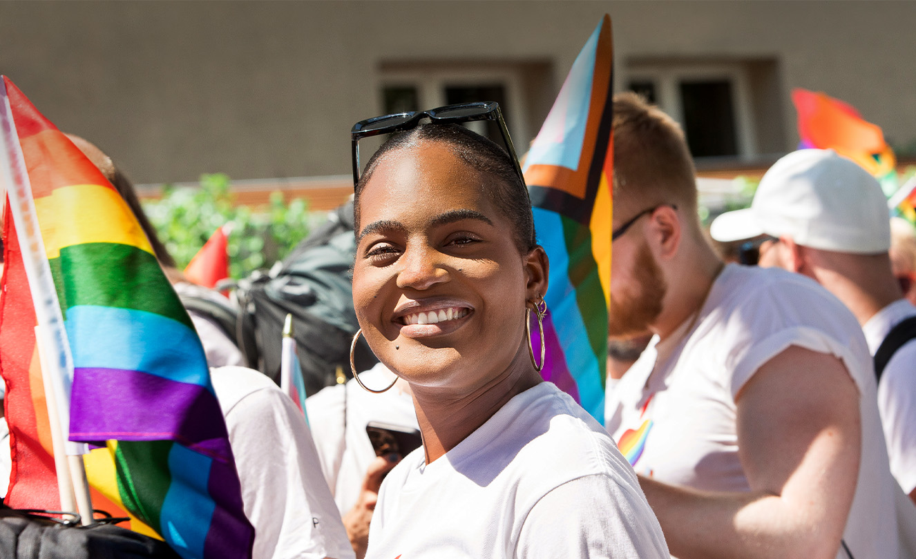 Funcionária sorri em um evento do Orgulho Apple junto com outros funcionários segurando bandeiras e usando camisetas do evento. 