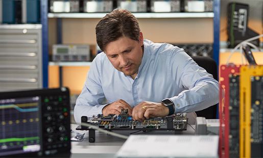 Greg trabalhando em um laboratório de engenharia de hardware, cercado de equipamentos de teste de chips.