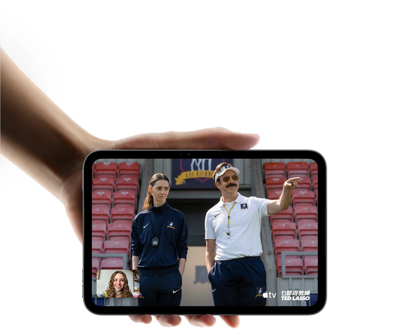 iPad mini in Midnight color, being held by a hand, displaying Apple TV Show, Ted Lasso being watched with SharePlay on a FaceTime call.