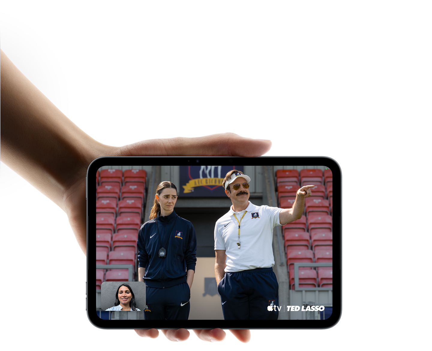 iPad mini in Midnight color, being held by a hand, displaying Apple TV Show, Ted Lasso being watched with SharePlay on a FaceTime call.