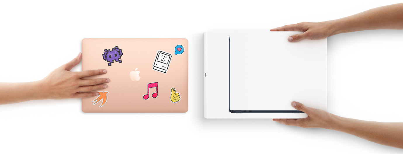Una mano acerca una MacBook con stickers en la cubierta hacia otras dos manos que sostienen una MacBook nueva dentro de su caja