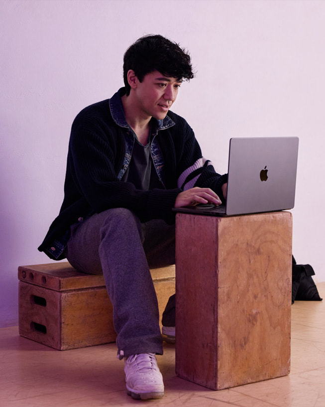 كايل هاناغامي يجلس على صندوق في استوديو، ويكتب على جهاز MacBook Pro موضوع على صندوق آخر.

