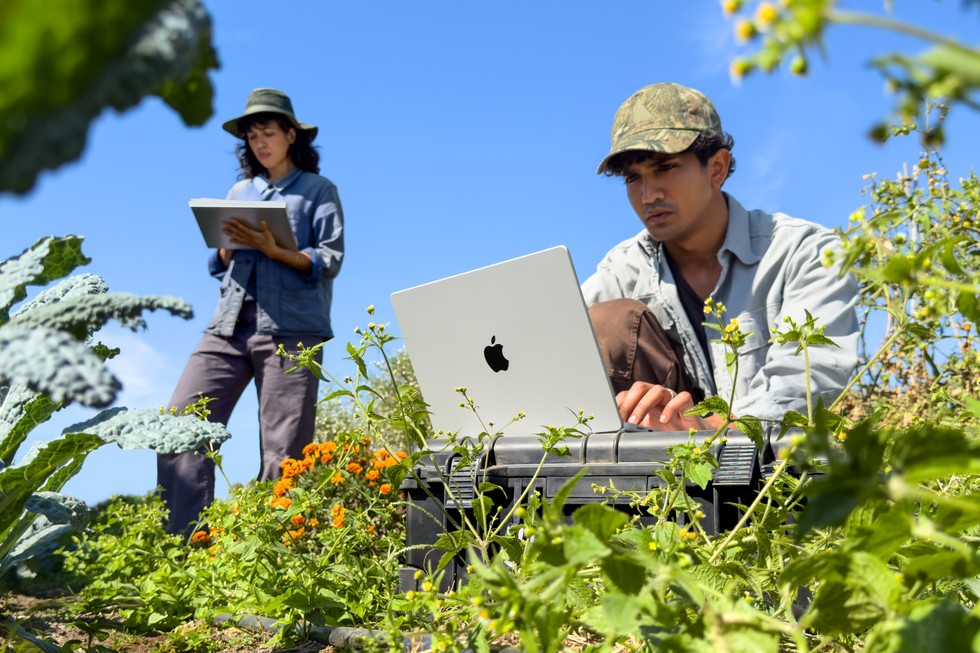 Zwei Personen arbeiten an einem sonnigen Tag im Freien mit einem MacBook Pro.