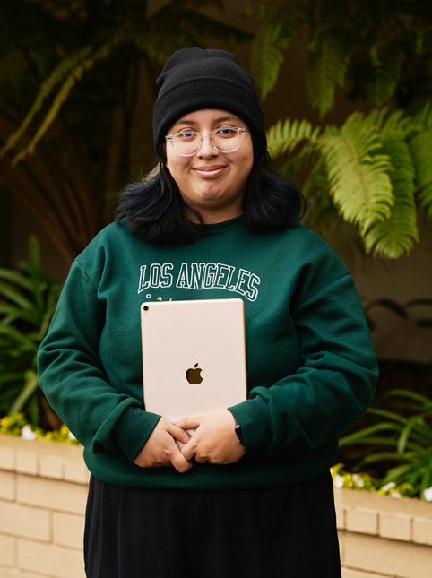 Et portræt af Angela Ibarra, en studerende hos Exceptional Minds. Angela har en grøn sweatshirt på med skriften “Los Angeles, California” samt klare briller og en sort hue.