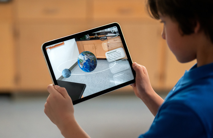 Un estudiante explora la realidad aumentada en el iPad, la pantalla muestra la luna orbitando la Tierra como si estuviera dentro del salón de clases