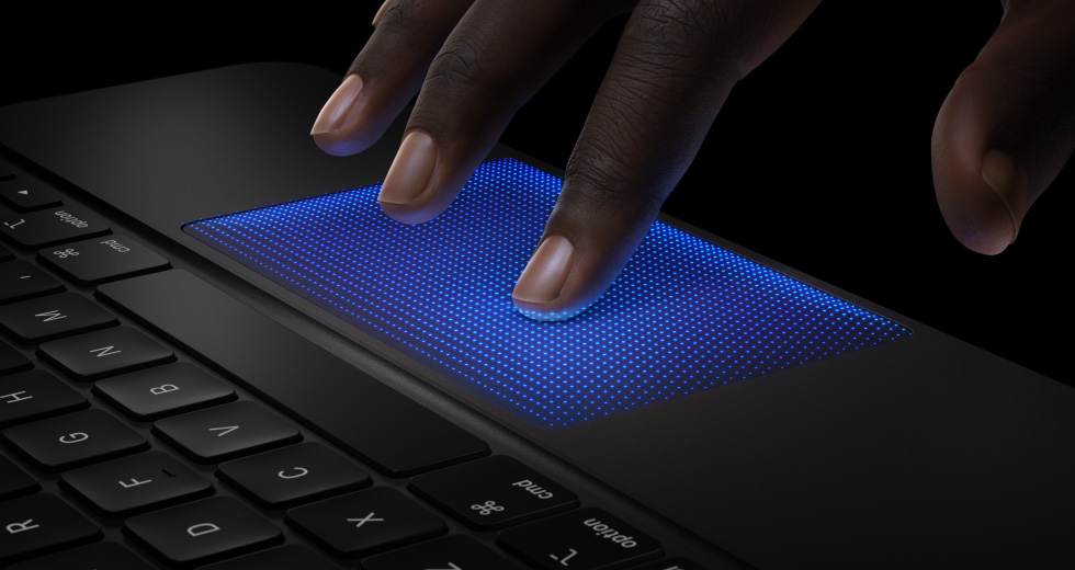 Animácia ruky s prstami vznášajúcimi sa nad trackpadom klávesnice Magic Keyboard, ukazovák s modrým tieňom predvádza akciu klepnutia s haptickou odozvou