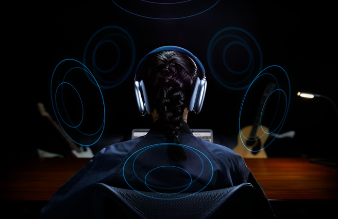 La testa di una persona che indossa un paio di Apple AirPods Max vista da dietro; elementi grafici attorno alla testa che indicano l’audio spaziale