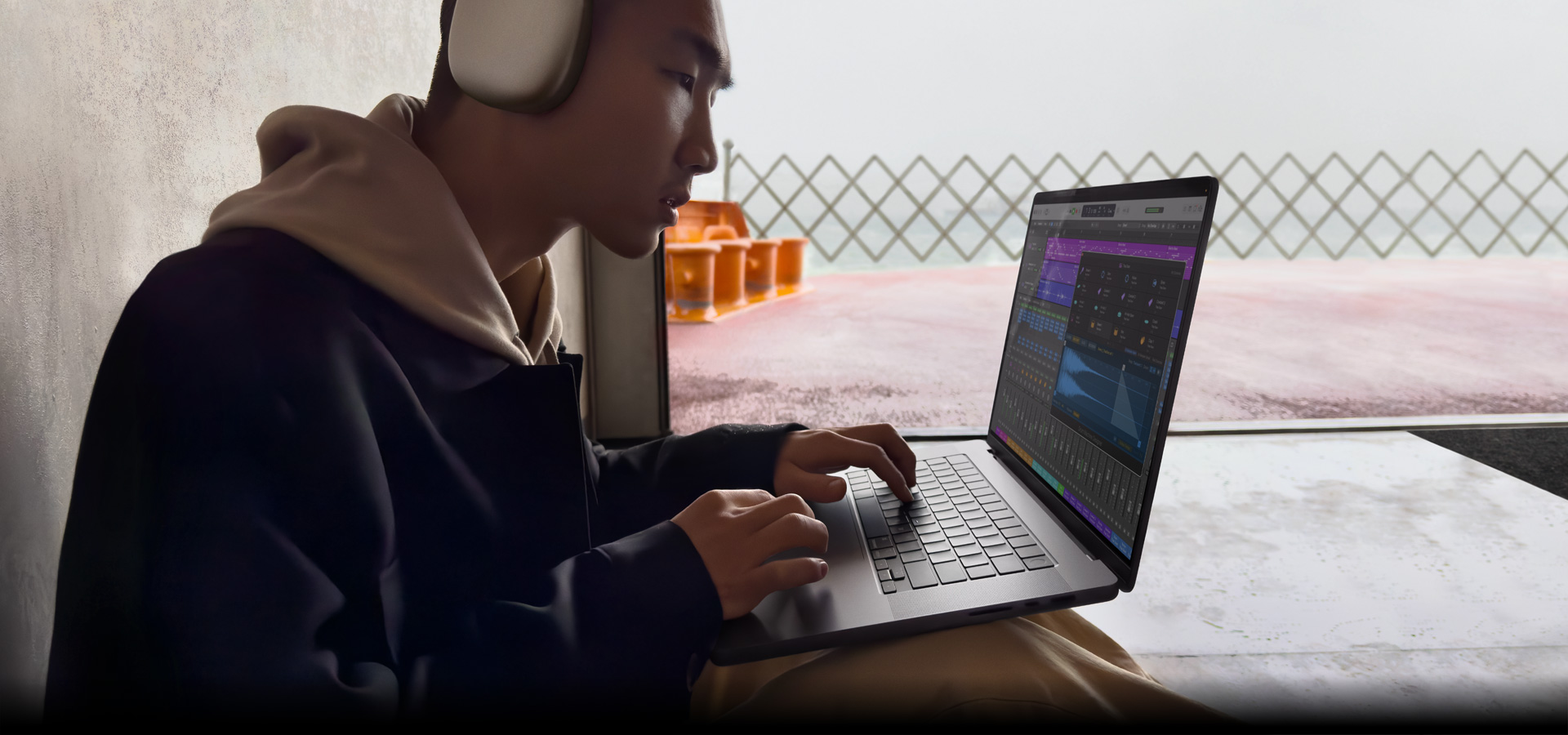 Una persona di profilo che indossa un paio di AirPods Max mentre usa Logic Pro su un MacBook Pro 16, lo schermo mostra lo spazio di lavoro di Logic Pro